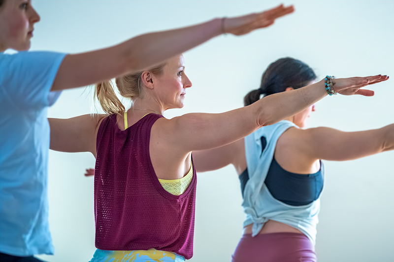 Gruppe Yogaschülerinnen Krieger 2 Yogaschülerin blickt über ausgestreckten Arm im Yogastudio Berlin