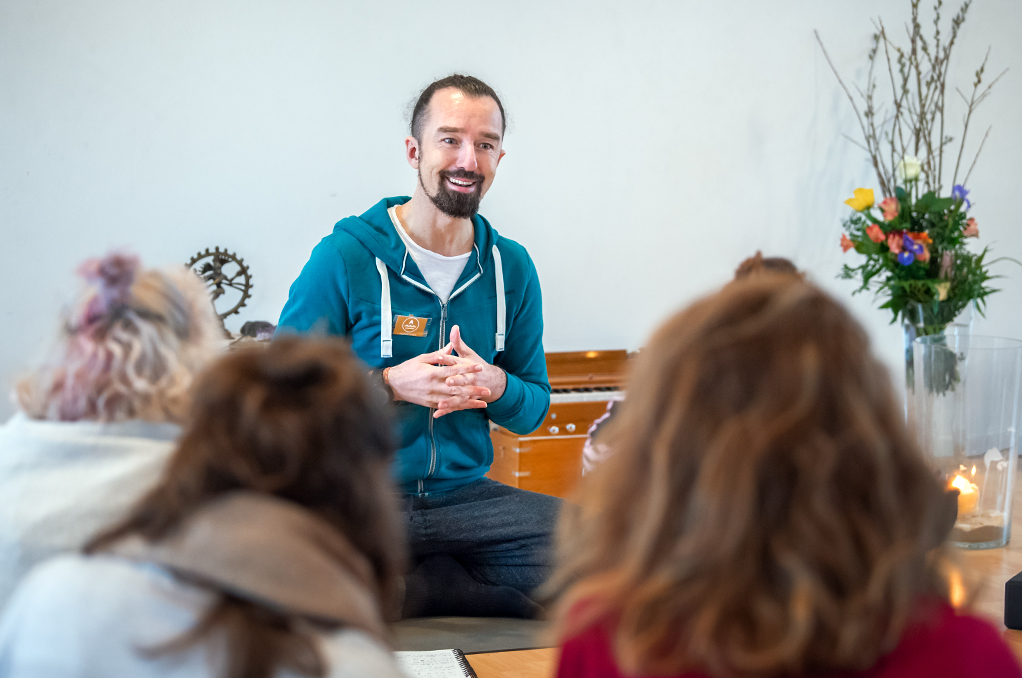 Alexander Kröker spricht vor Yogalehrerinnen Gruppe im Yogastudio bei einer Ausbildung Berlin im Hintergrund Altar, Blumen und Harmonium