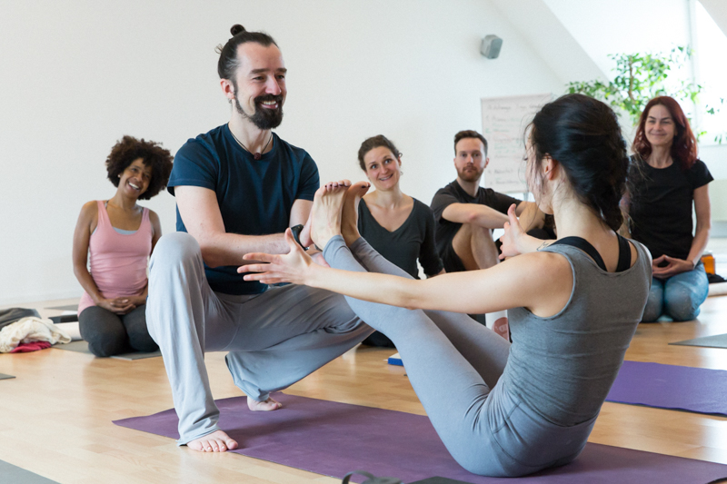 Alexander Kröker mit Gruppe Yogaschülerinnen und Yogaschülern im großen Raum im Yogastudio bei einer Ausbildung Berlin
