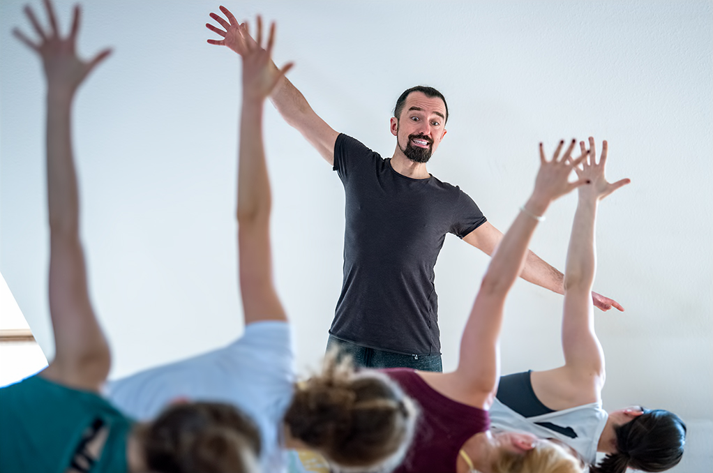Alexander Kröker streckt die Arme aus und unterrichtet Yoga vor Gruppe MethodeBerlin-Yoga-Conference-PoUp-Element-OliverEuleYoga Ausbildung mit Schuelerin lachend